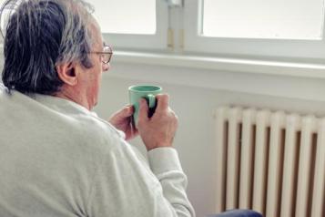 Man sits by radiator holding mug