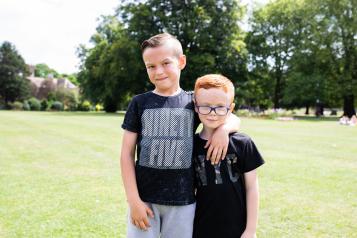 two boys stood in the park with their arms round each other