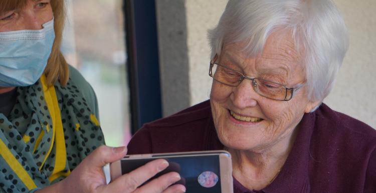 younger woman wearing a mask showing an older woman a phone 