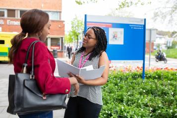 Photo shows two women talking outside of a hospital. 