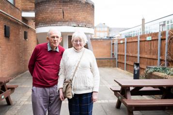 two older people standing outside looking into camera