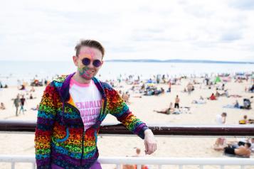 man wearing multicoloured face paint stood in front of a beach