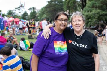 Two women, one has arm round second, who is wearing a rainbow T shirt