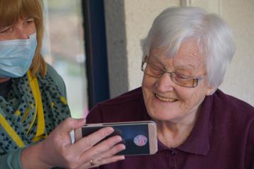 younger woman wearing a mask showing an older woman a phone 