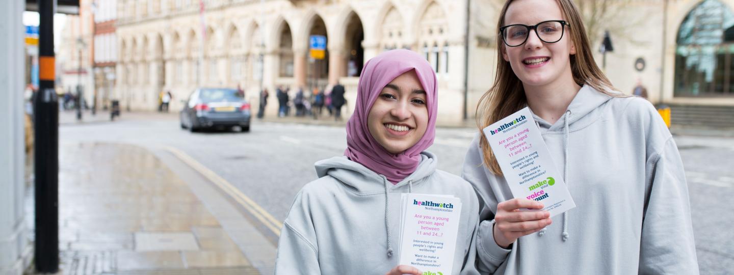 Two young female volunteers holding Healthwatch leaflets